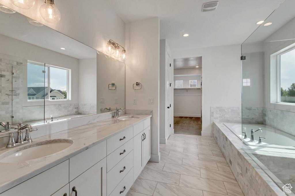 Bathroom with healthy amount of natural light, double vanity, a garden tub, recessed lighting, and marble finish flooring