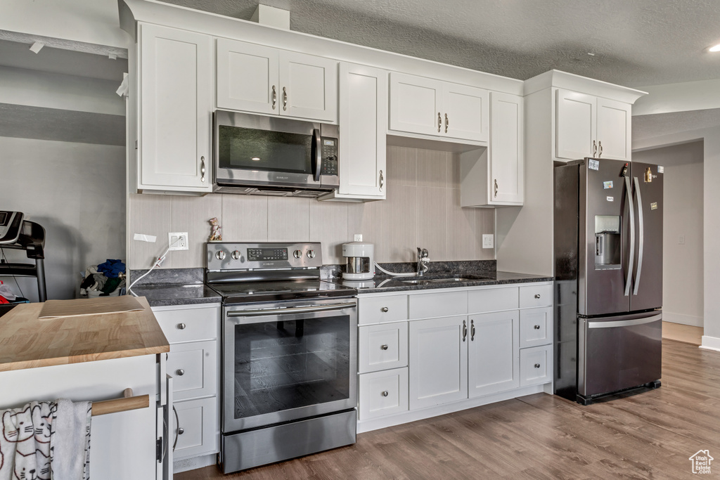 Kitchen with appliances with stainless steel finishes, wood finished floors, white cabinets, dark stone countertops, and a textured ceiling