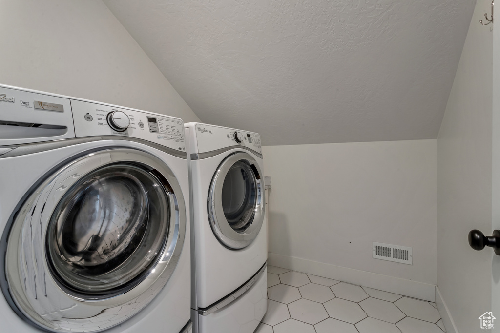 Washroom with independent washer and dryer, a textured ceiling, and light tile patterned floors