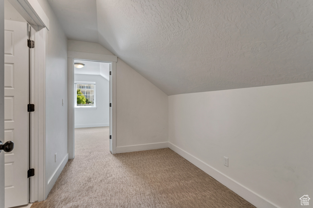 Additional living space featuring a textured ceiling, vaulted ceiling, and carpet floors