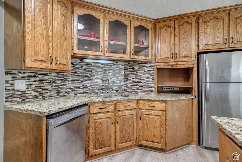 Kitchen featuring stainless steel appliances, backsplash, glass insert cabinets, and light stone countertops