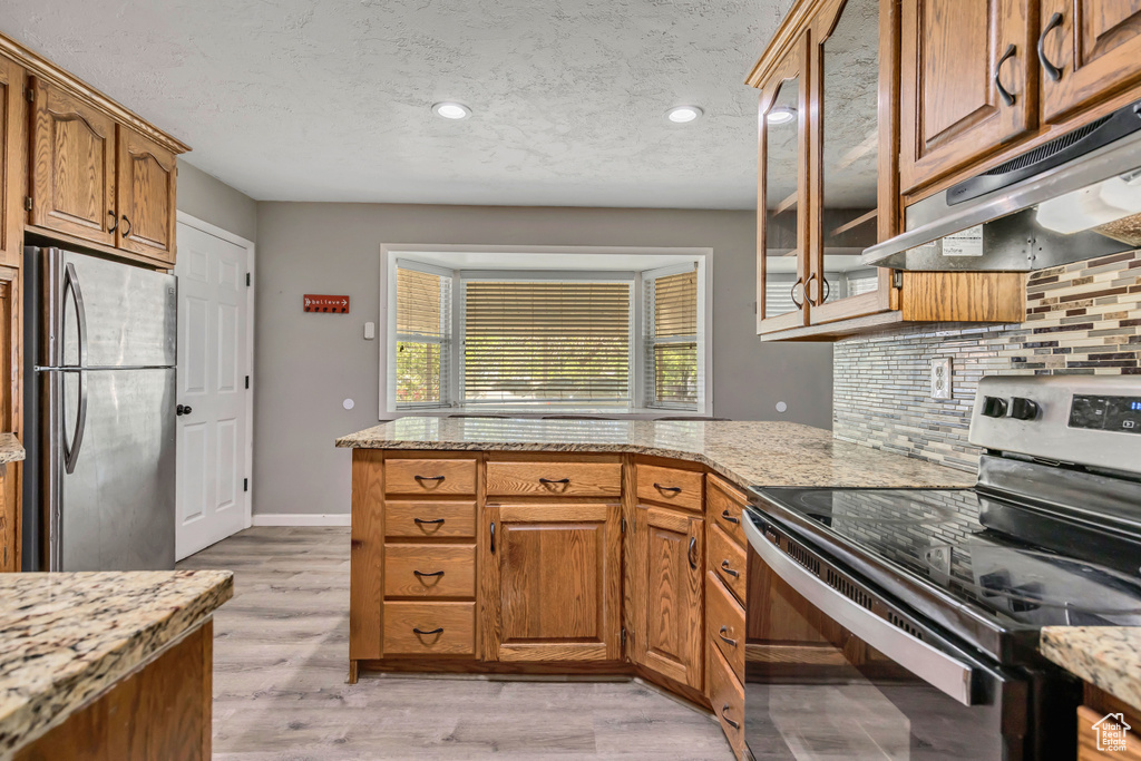 Kitchen with stainless steel appliances, backsplash, under cabinet range hood, glass insert cabinets, and a peninsula