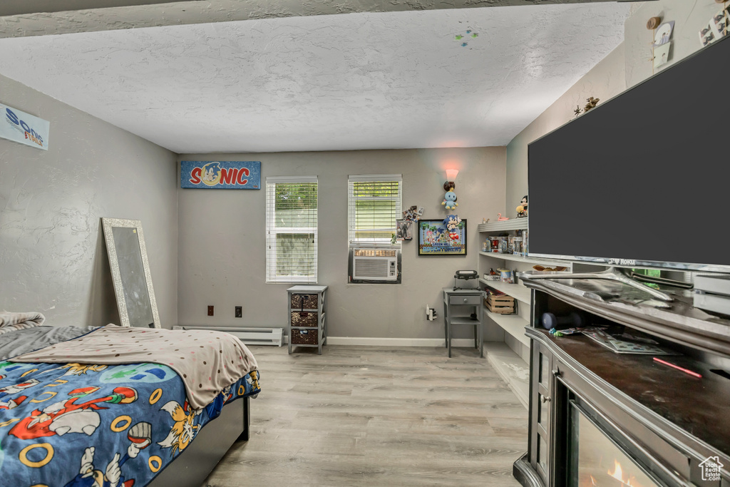 Bedroom featuring light wood finished floors, a textured ceiling, a baseboard heating unit, and cooling unit