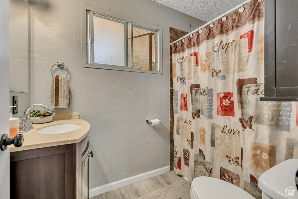 Bathroom with vanity, wood finished floors, a textured ceiling, curtained shower, and a textured wall