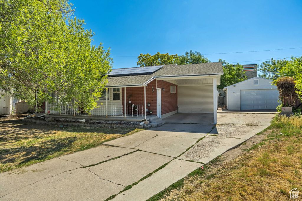 Ranch-style house with a porch, a shingled roof, solar panels, driveway, and an outdoor structure