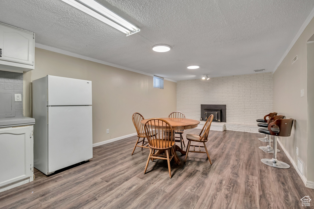 Dining area featuring a fireplace, wood finished floors, a textured ceiling, and ornamental molding