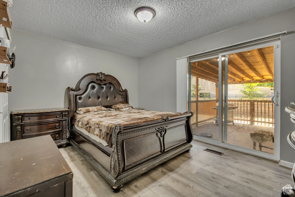Bedroom featuring access to exterior, light wood-type flooring, and a textured ceiling