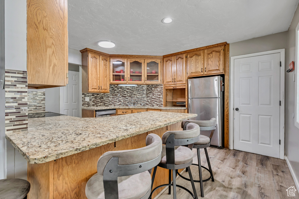 Kitchen featuring a peninsula, a kitchen breakfast bar, freestanding refrigerator, glass insert cabinets, and light stone counters