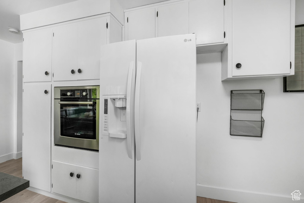 Kitchen featuring white refrigerator with ice dispenser, oven, wood finished floors, and white cabinets