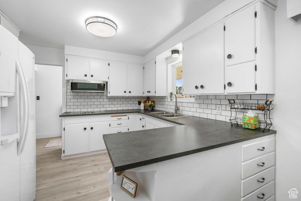Kitchen with white fridge with ice dispenser, dark countertops, white cabinets, decorative backsplash, and light wood-style floors