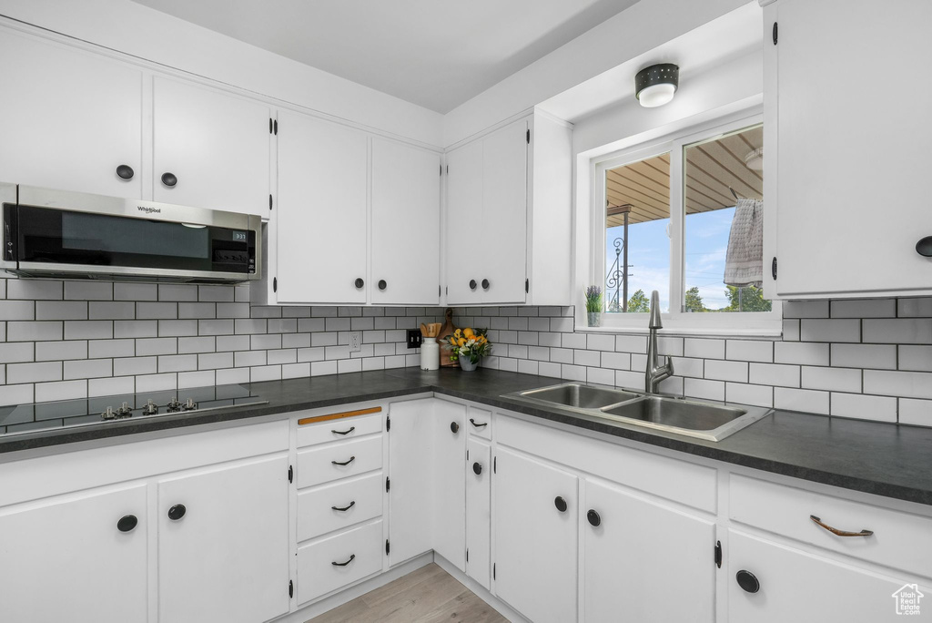 Kitchen with dark countertops, white cabinetry, tasteful backsplash, black electric cooktop, and stainless steel microwave