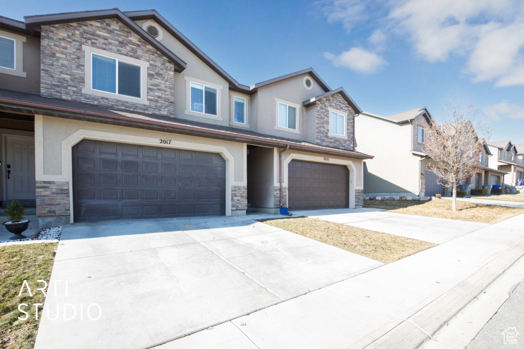 View of front of property featuring stone siding, an attached garage, stucco siding, and driveway