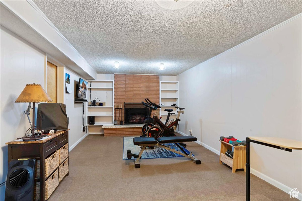 Exercise room with a textured ceiling, a brick fireplace, light colored carpet, and ornamental molding