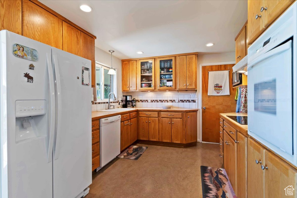 Kitchen featuring white appliances, backsplash, light countertops, glass insert cabinets, and brown cabinets