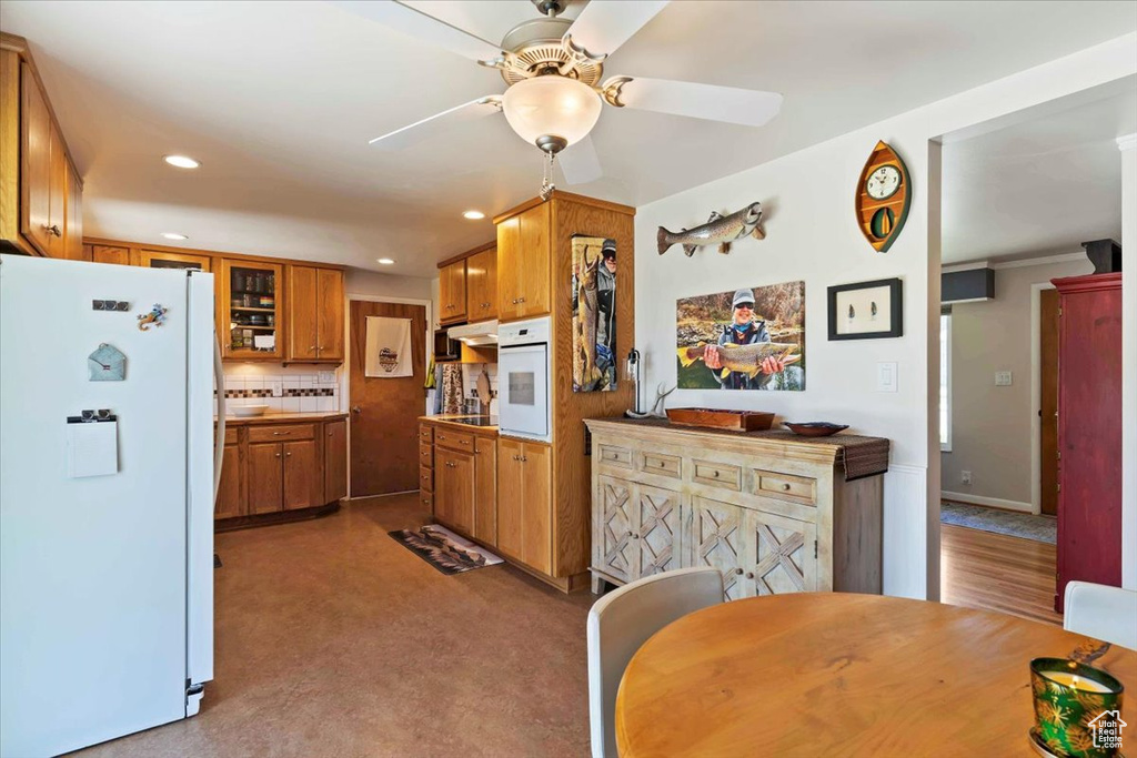 Kitchen featuring white appliances, brown cabinetry, ceiling fan, backsplash, and recessed lighting