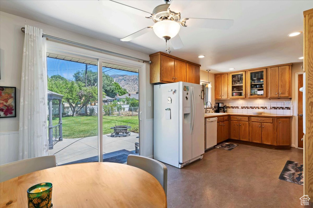 Kitchen featuring white appliances, tasteful backsplash, glass insert cabinets, brown cabinetry, and light countertops