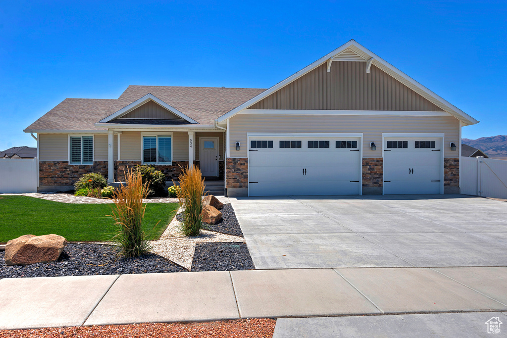 Craftsman-style home featuring a garage, stone siding, a shingled roof, driveway, and covered porch