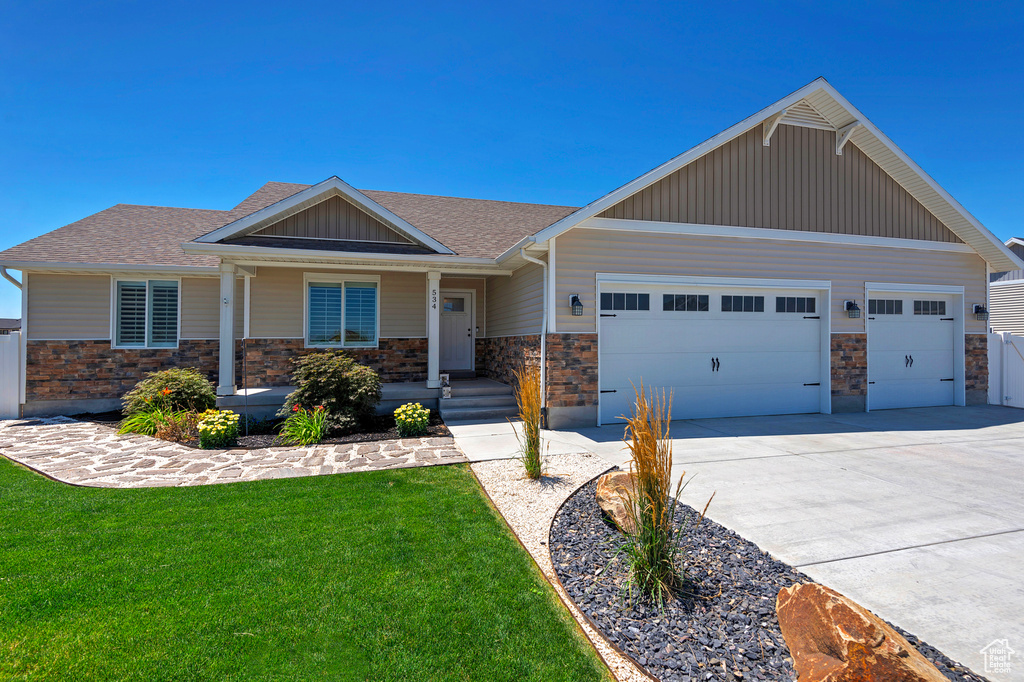 Craftsman inspired home featuring a shingled roof, a garage, a front lawn, driveway, and stone siding