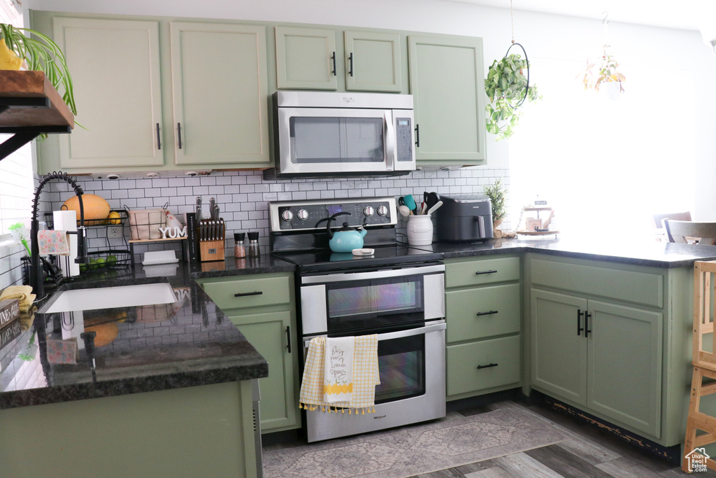 Kitchen with green cabinetry, appliances with stainless steel finishes, decorative backsplash, dark stone countertops, and a chandelier