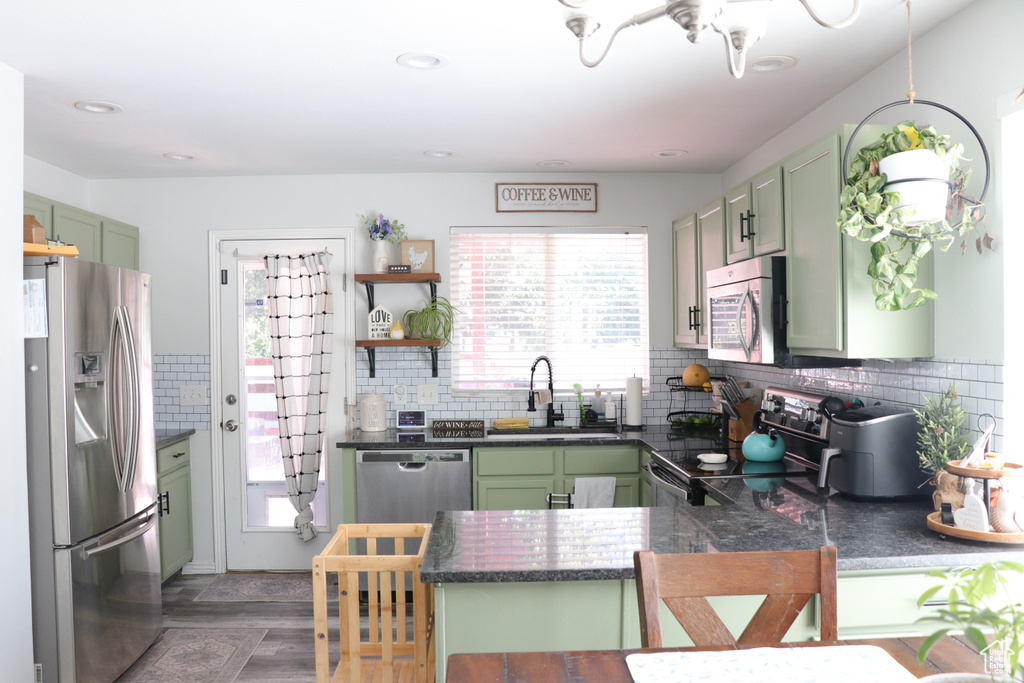 Kitchen with green cabinetry, stainless steel appliances, a peninsula, dark countertops, and decorative backsplash