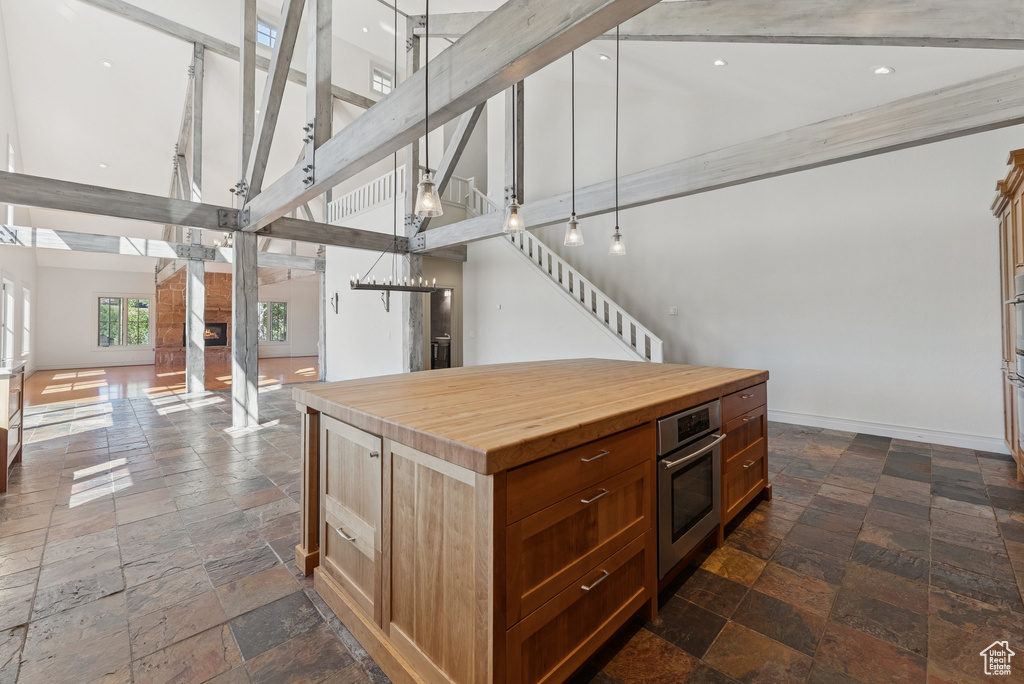 Kitchen with open floor plan, a towering ceiling, stone tile flooring, wooden counters, and a center island