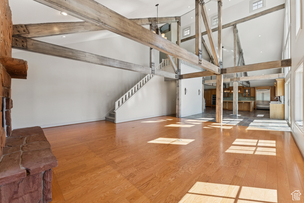 Unfurnished living room featuring high vaulted ceiling, beamed ceiling, wood finished floors, and stairs