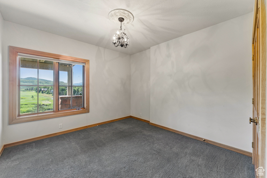Unfurnished room featuring a chandelier and dark colored carpet