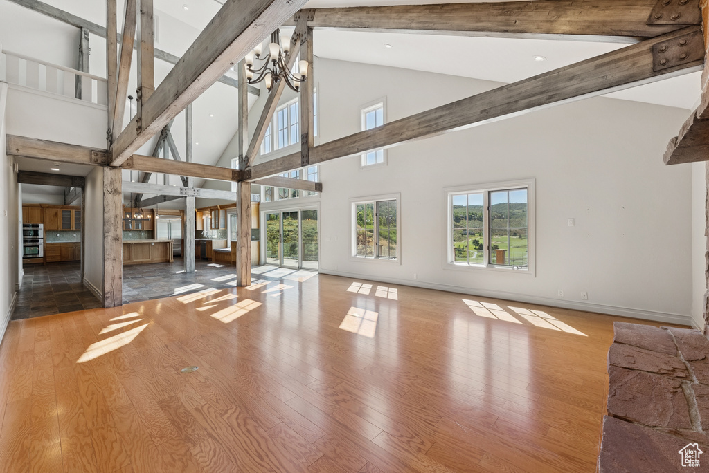 Unfurnished living room with high vaulted ceiling, beamed ceiling, wood finished floors, and a chandelier
