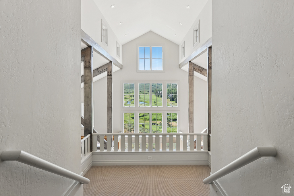 Stairway featuring carpet floors, a textured wall, and high vaulted ceiling