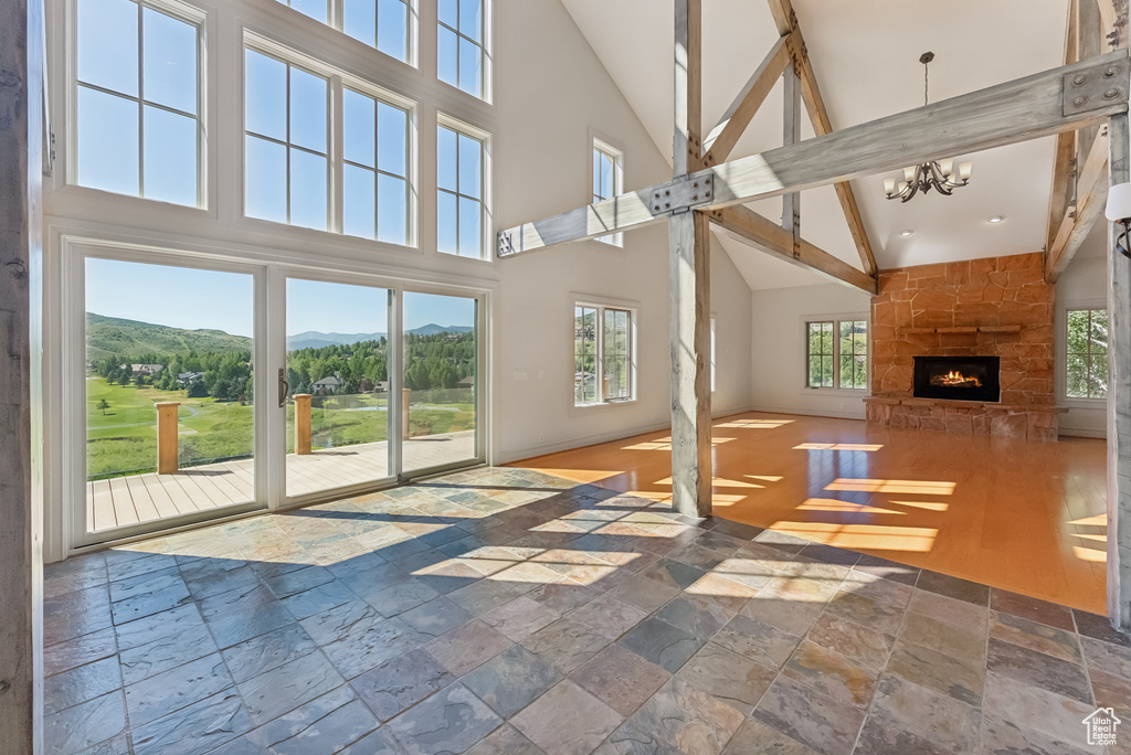 Unfurnished living room with high vaulted ceiling, stone tile flooring, a mountain view, a stone fireplace, and a chandelier