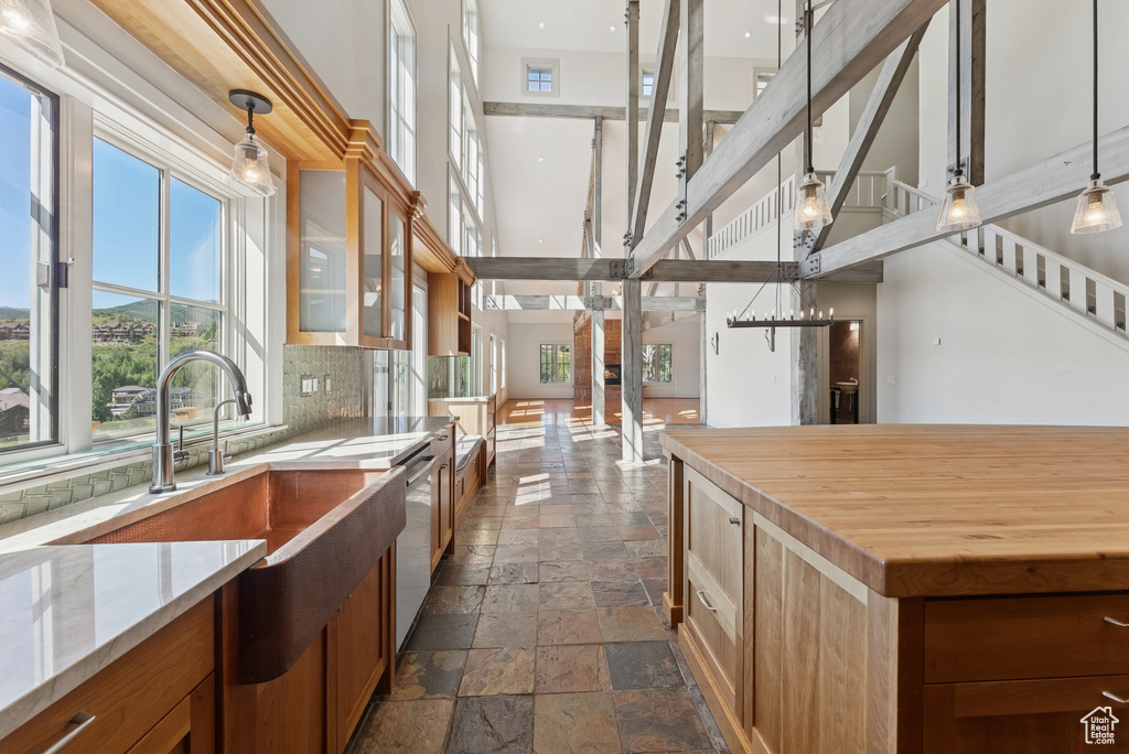 Kitchen featuring stone tile floors, a towering ceiling, tasteful backsplash, brown cabinets, and decorative light fixtures
