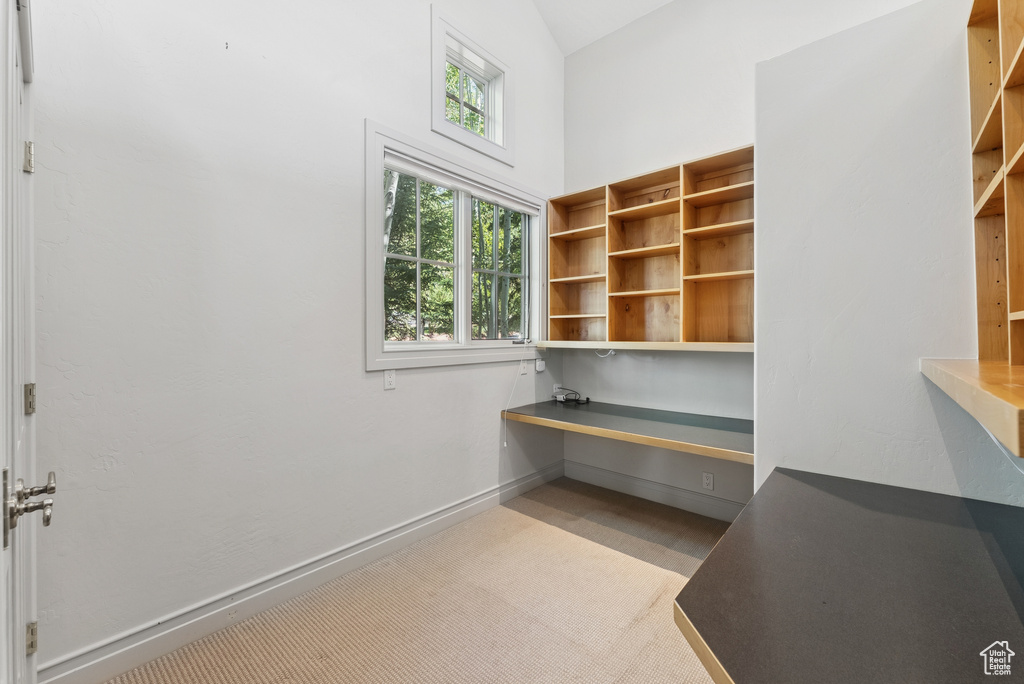 Unfurnished office with built in desk, carpet floors, and high vaulted ceiling