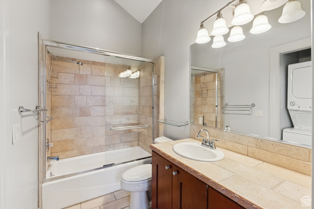 Bathroom with stacked washer / drying machine, vanity, and shower / bath combination with glass door