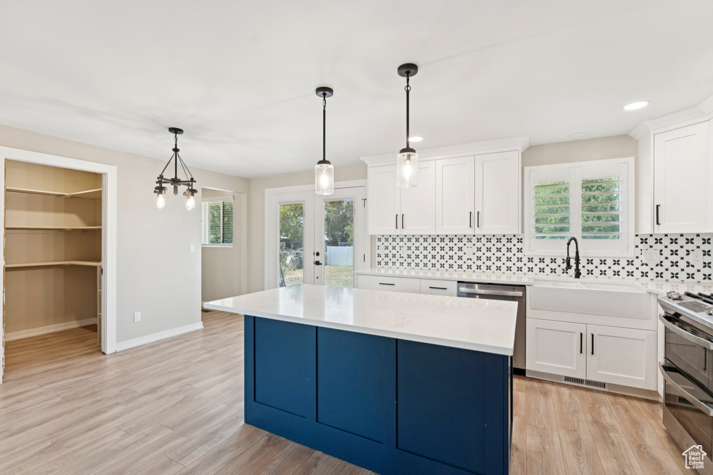 Kitchen with backsplash, light countertops, stainless steel appliances, white cabinets, and a center island