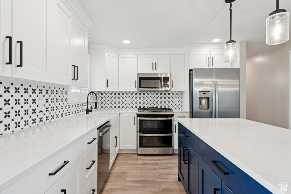 Kitchen with recessed lighting, stainless steel appliances, white cabinetry, light wood-style floors, and hanging light fixtures