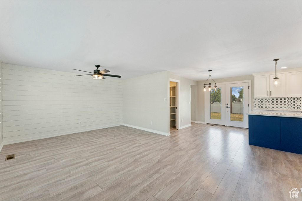 Unfurnished living room featuring light wood finished floors, ceiling fan, french doors, and a chandelier