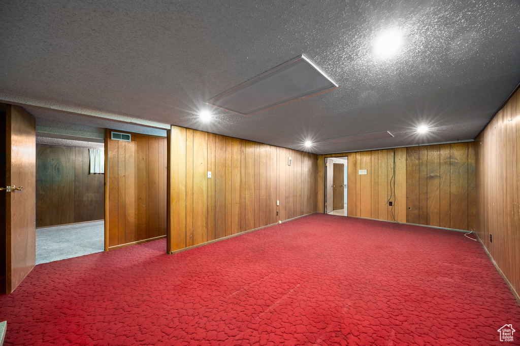 Finished basement with carpet floors, a textured ceiling, and wood walls