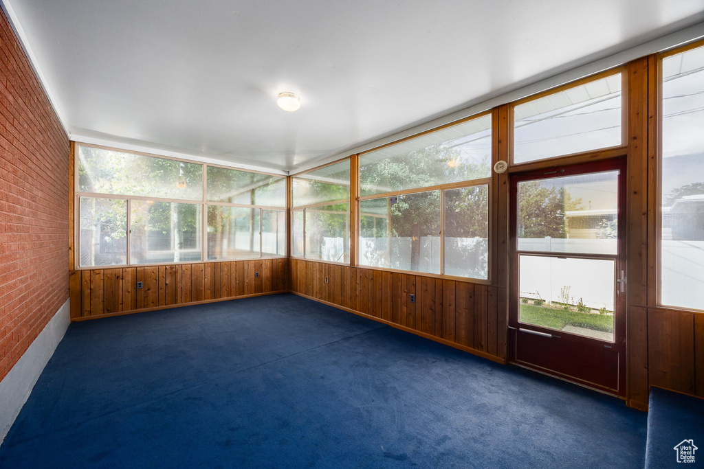 Unfurnished sunroom with brick wall, carpet floors, and wooden walls