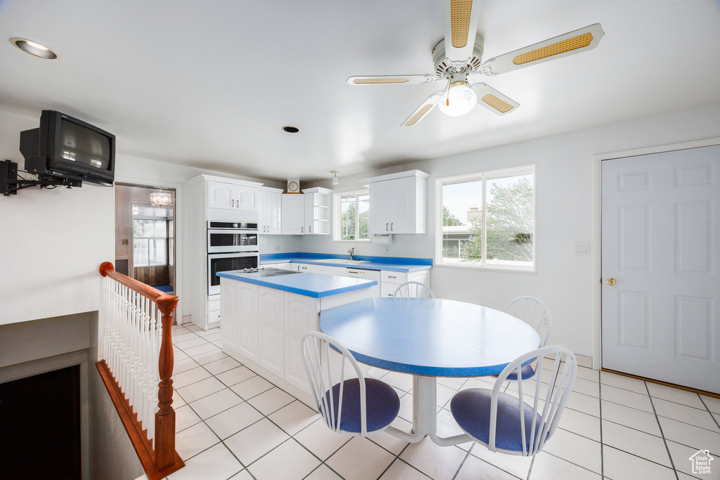 Kitchen featuring light tile patterned floors, white cabinetry, ceiling fan, stainless steel double oven, and a center island