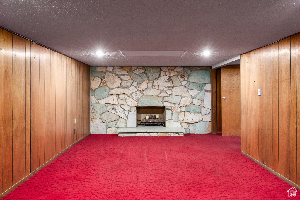 Unfurnished living room featuring wood walls, a stone fireplace, and carpet floors