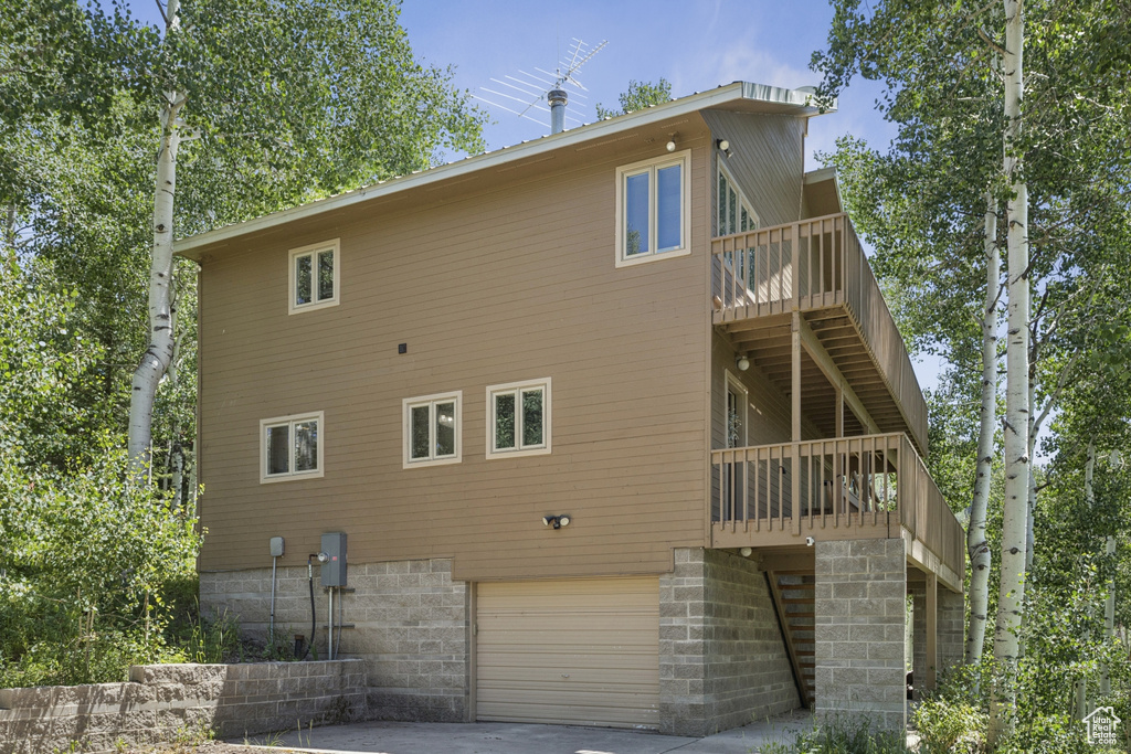 Rear view of house with an attached garage, a deck, and concrete driveway