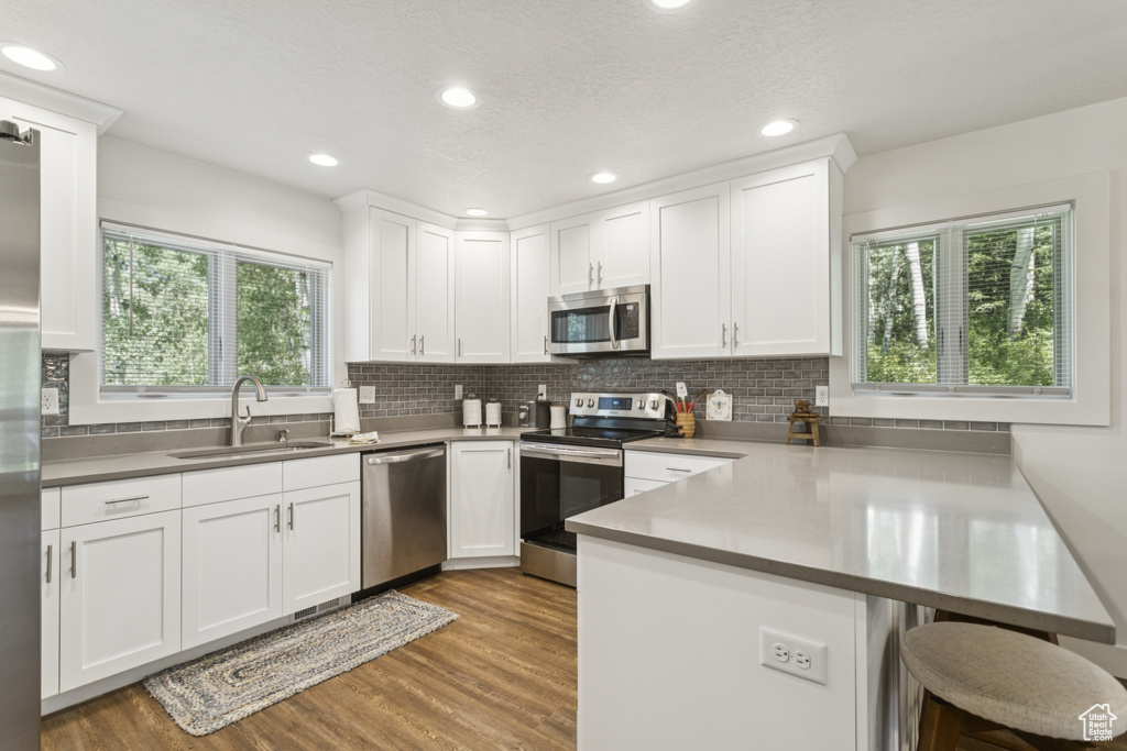 Kitchen with a peninsula, stainless steel appliances, white cabinets, wood finished floors, and decorative backsplash