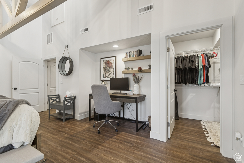 Bedroom with a spacious closet, dark wood-type flooring, a desk, and a high ceiling
