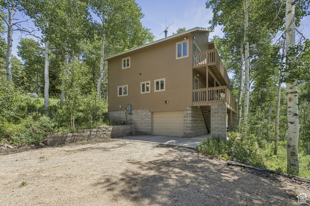 Back of property featuring an attached garage, dirt driveway, and a deck