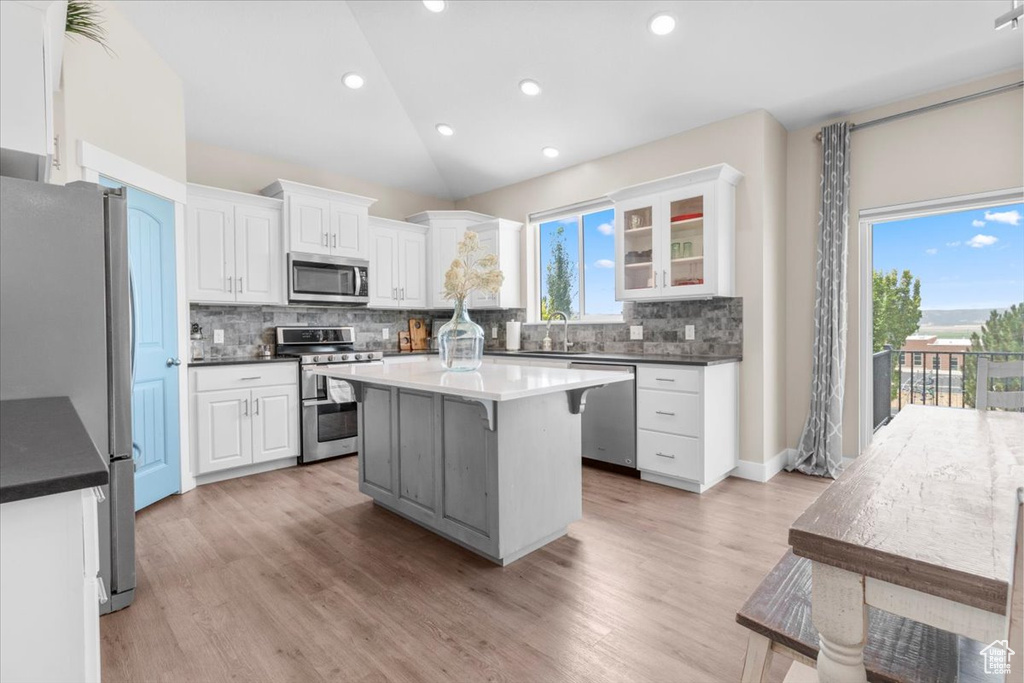 Kitchen with appliances with stainless steel finishes, decorative backsplash, white cabinets, vaulted ceiling, and a center island