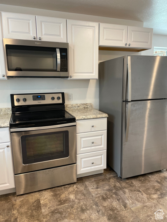 Kitchen featuring stainless steel appliances, white cabinets, stone finish flooring, and light stone counters