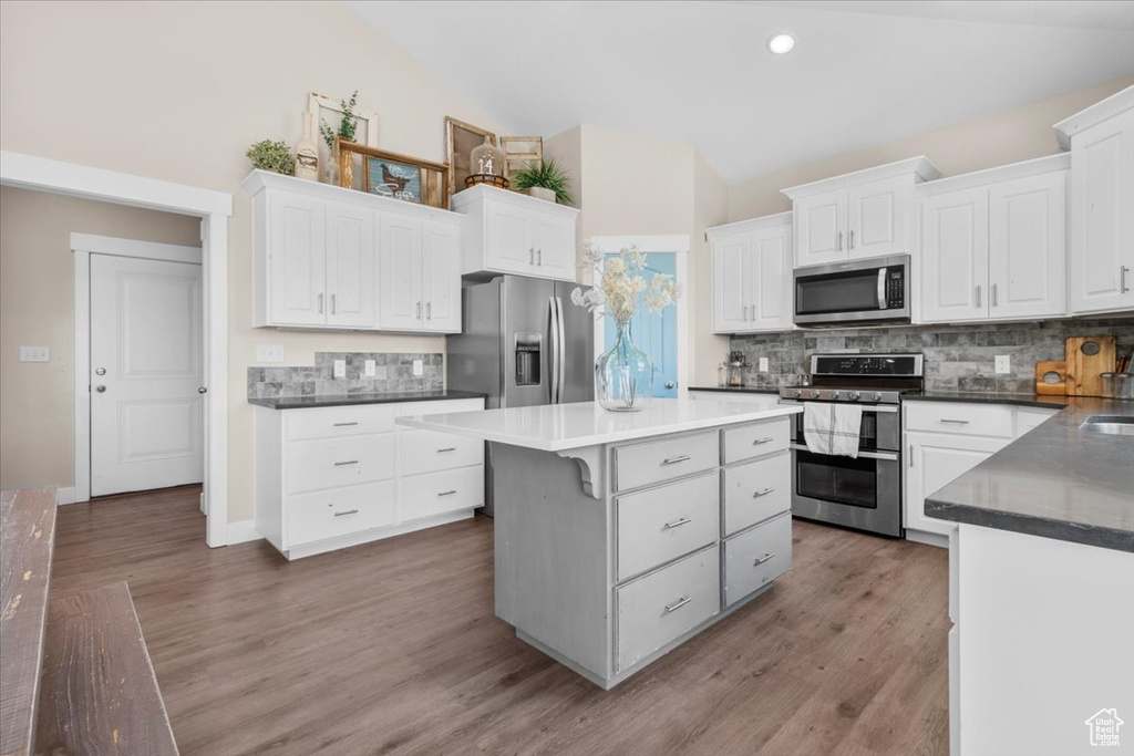 Kitchen featuring appliances with stainless steel finishes, backsplash, a center island, white cabinetry, and dark countertops