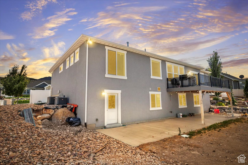 Back of property at dusk with a patio area, stucco siding, and a balcony
