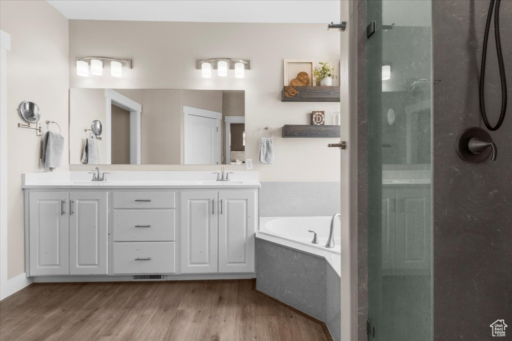 Full bath featuring a stall shower, a garden tub, and wood finished floors