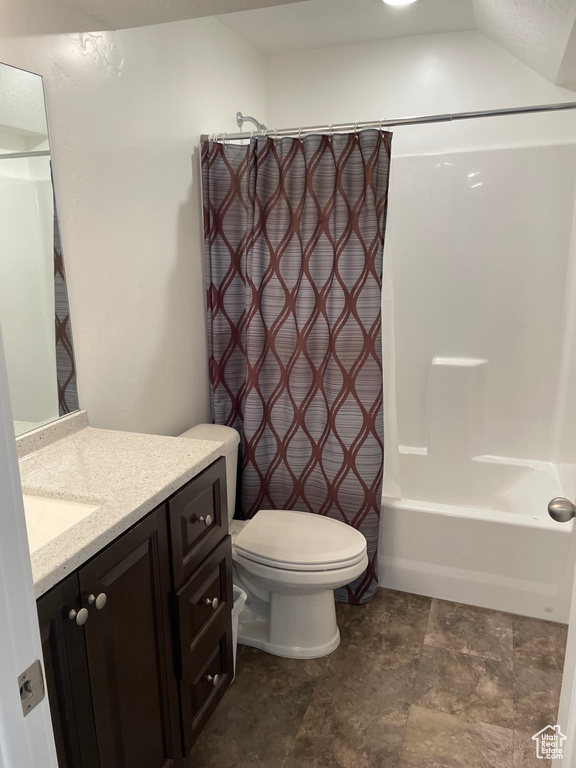 Bathroom featuring vanity, shower / bathtub combination with curtain, and stone finish flooring